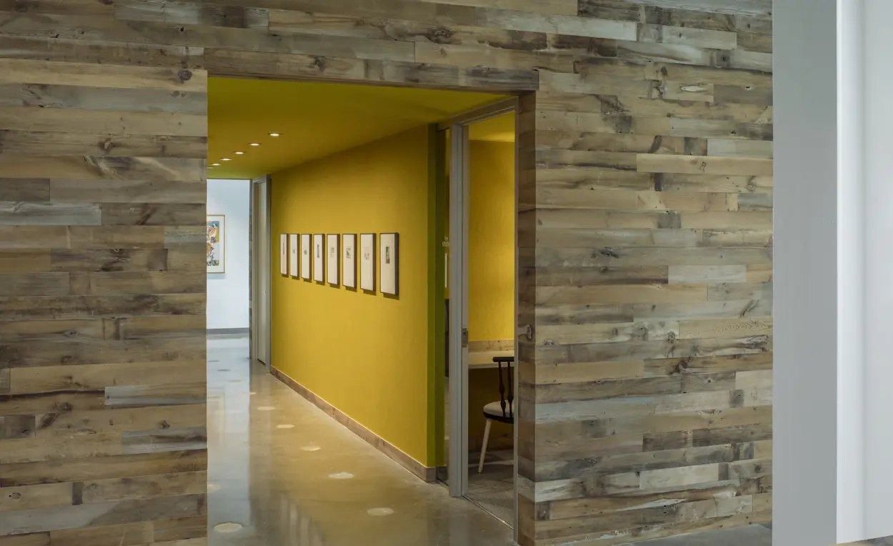 3M: Doorway in a reclaimed-wood wall leading to a yellow corridor