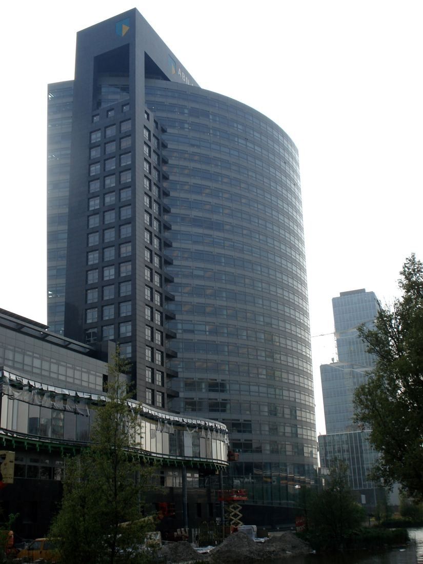 ABN AMRO: Curved glass tower with lower buildings and trees in front