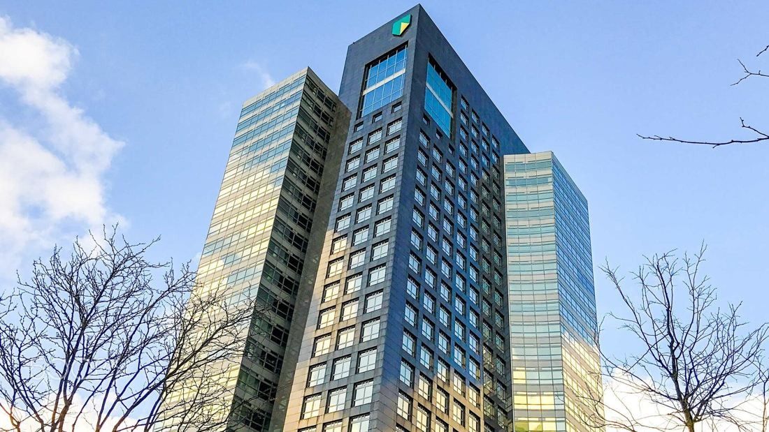 ABN AMRO: Dark granite tower flanked by reflective glass towers, seen from below between bare trees