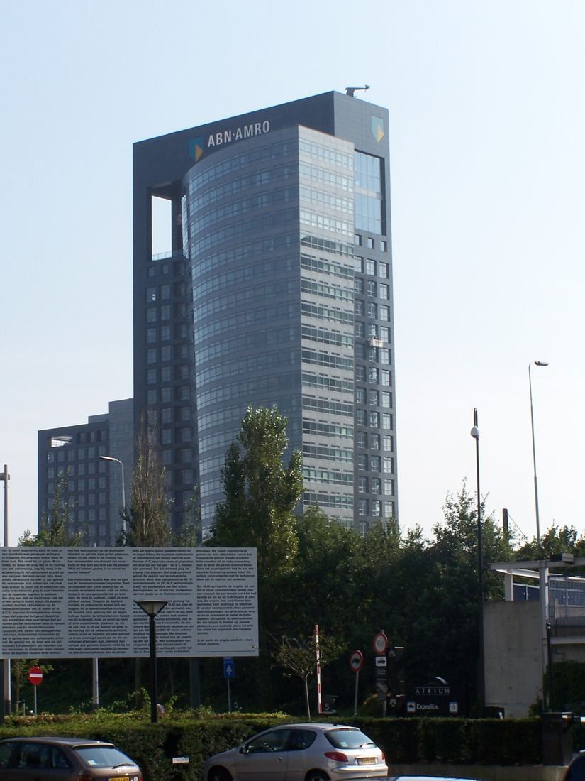 ABN AMRO: Dark tower with a glass top over trees and parked cars