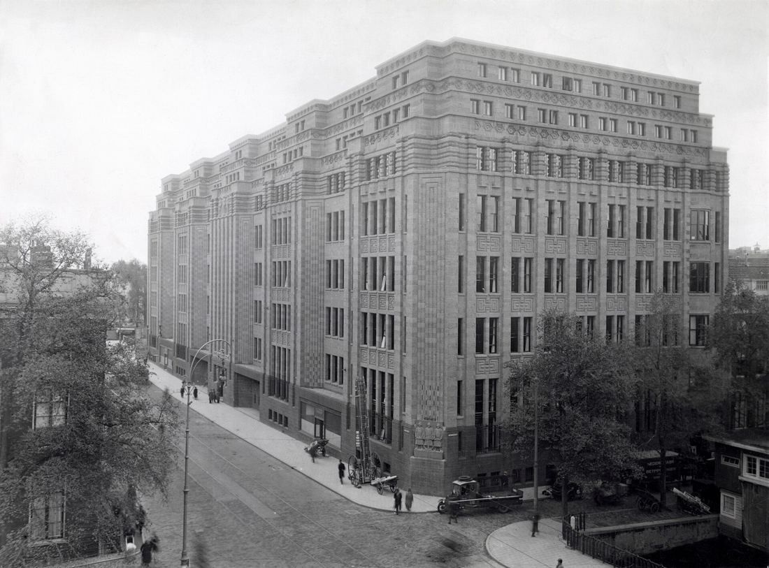 Large brick office block with many windows on a street corner, black and white