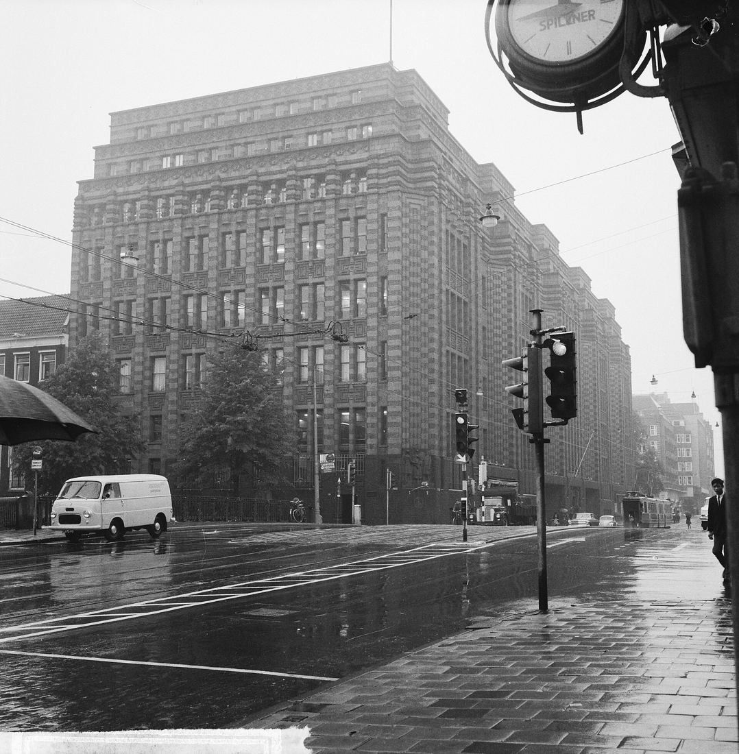 Large brick office building at a wet street crossing with traffic lights, black and white