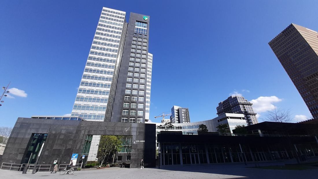 ABN AMRO: Tall pale tower behind a low dark granite building on a paved square