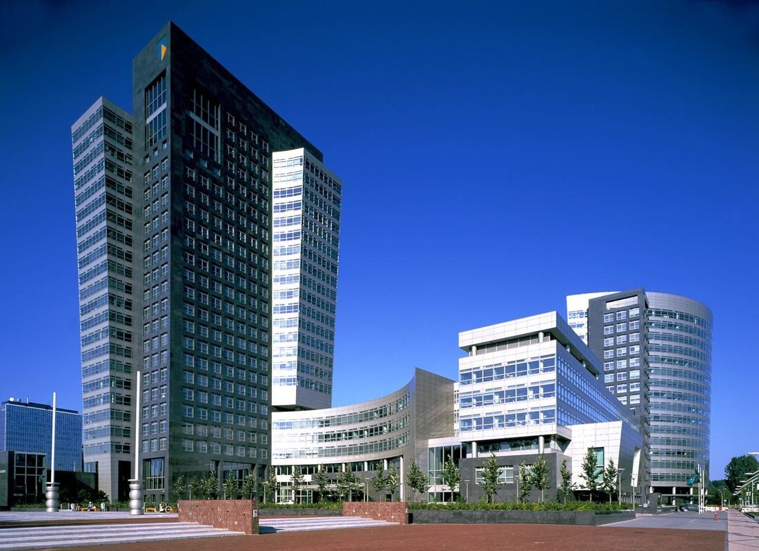 Two dark and pale glass towers rising above low curved office wings under a deep blue sky