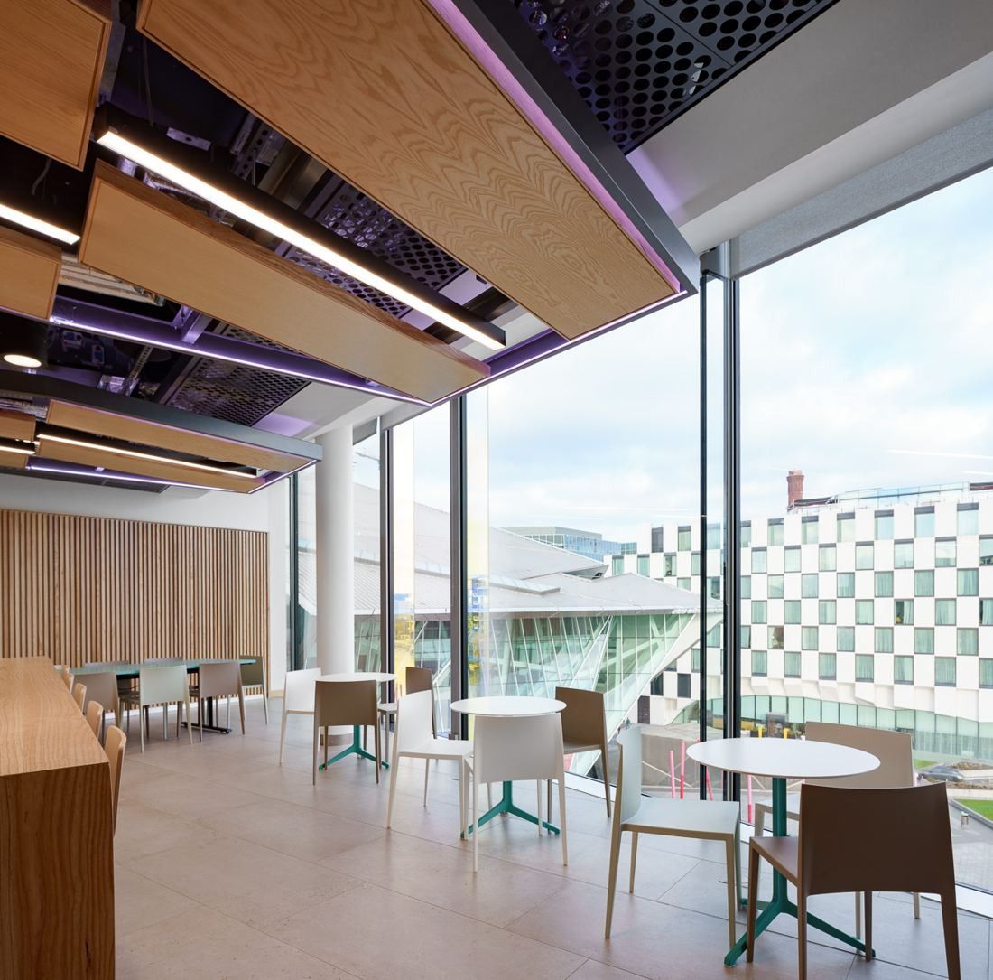 Accenture: Bright café area with round tables, wood-clad ceiling panels and floor-to-ceiling windows over the docklands