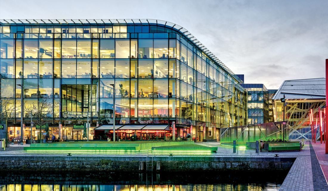 Accenture: Glass office building lit from inside at dusk, seen across the water of the dock