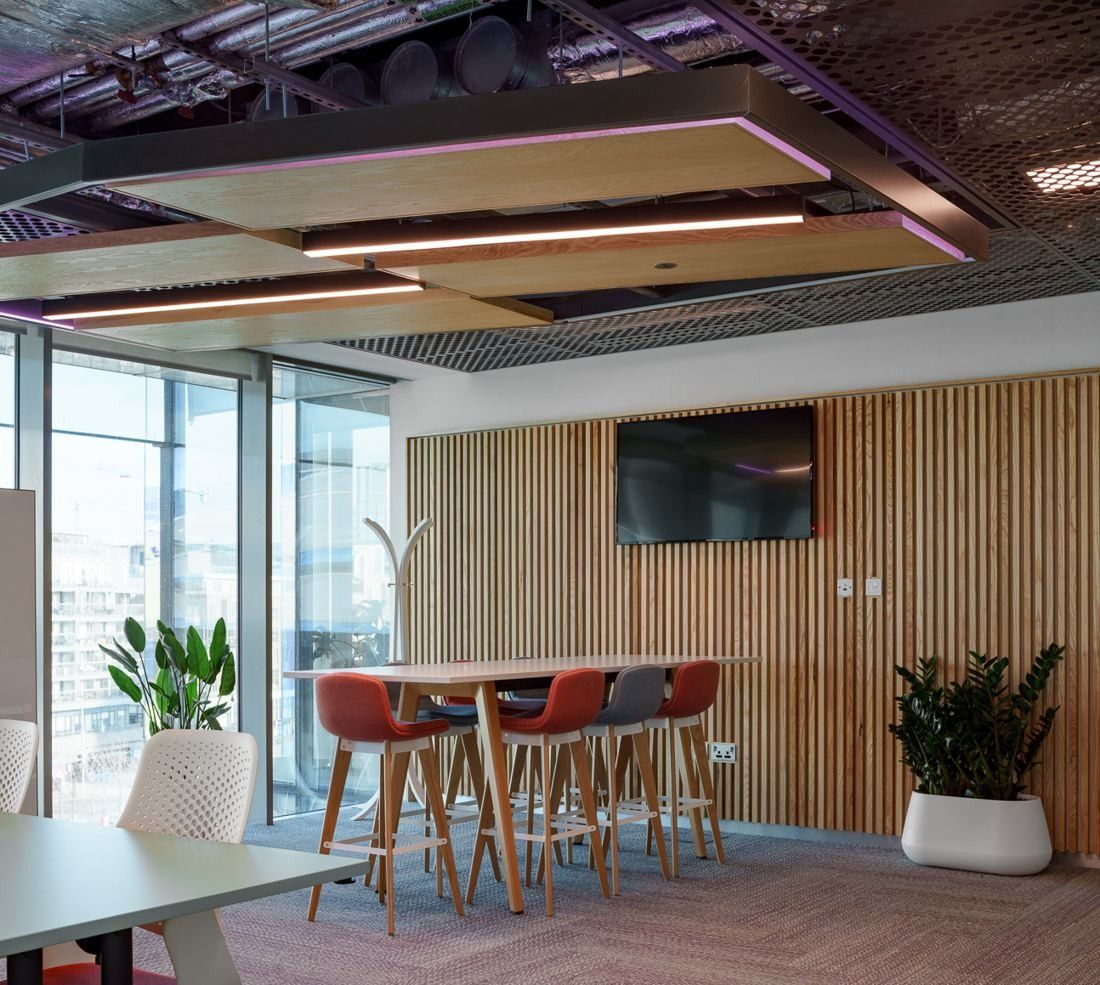 Accenture: High table with orange stools in front of a slatted timber wall and a screen, plants by the window