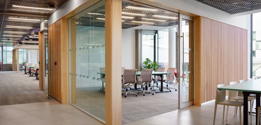 Accenture: Office floor with glass meeting rooms framed in light wood and work tables by the windows