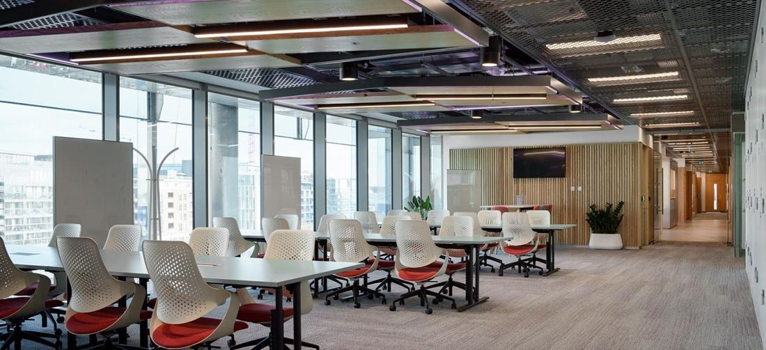 Accenture: Open office floor with rows of desks and red chairs along a glass wall with city views