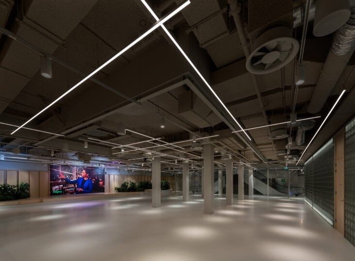 Adyen: Dark open floor with linear ceiling lights and a large screen