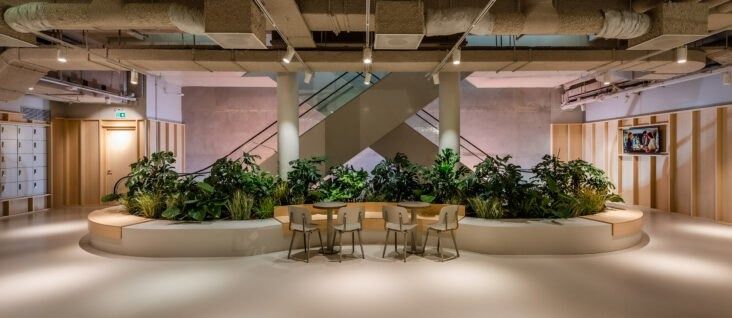 Adyen: Seating area with tables surrounded by planters under an exposed ceiling