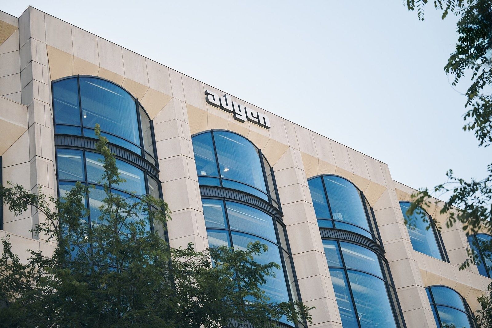 Stone facade with tall arched glass windows and the company name, trees in front