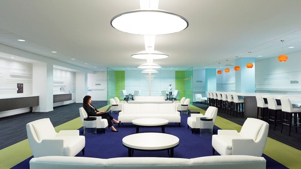 A bright lounge with white sofas, round tables and green and orange accents under a round light
