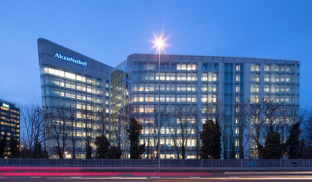 AkzoNobel: Long glass office block with the AkzoNobel name on top, lit at dusk with light trails in front