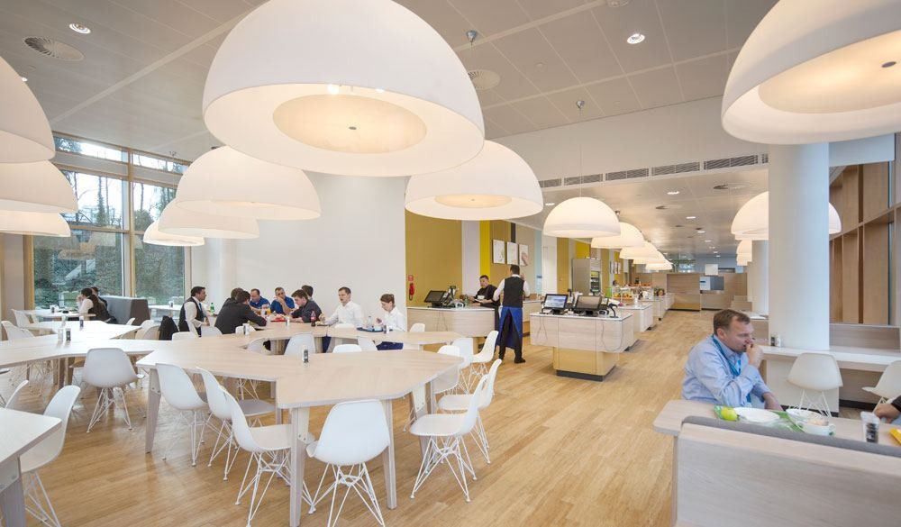 AkzoNobel: Restaurant hall with dome-shaped pendant lamps and long white tables by tall windows