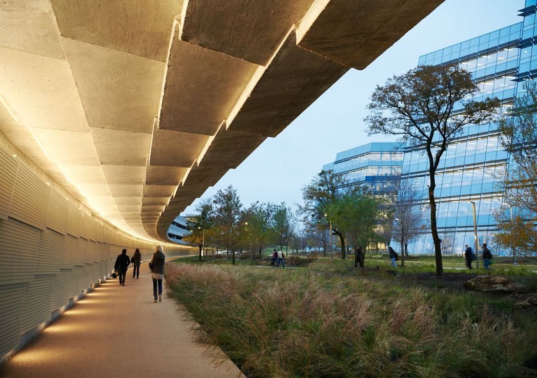 American Airlines: Covered walkway with a lit concrete canopy beside tall grasses and glass buildings