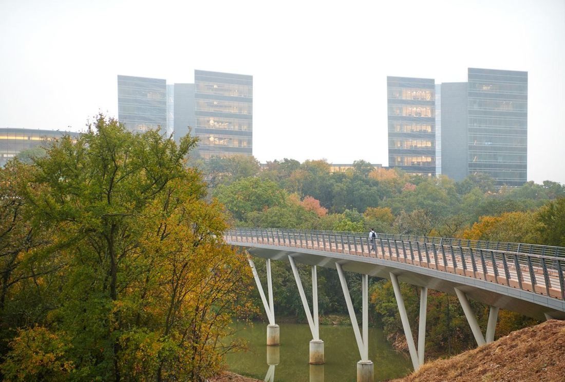 American Airlines: Pedestrian bridge over a creek with office towers behind autumn trees