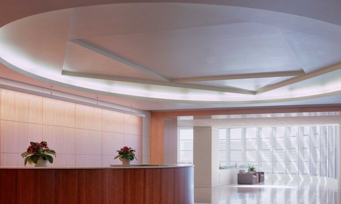 Amgen: Bright reception area with a curved wooden desk under an oval recessed ceiling and a glass-block wall