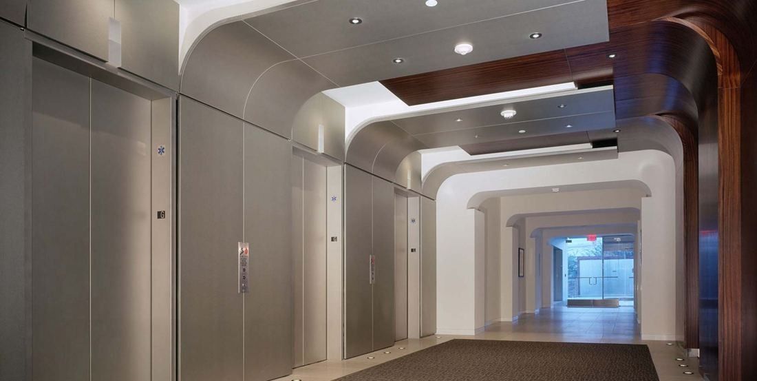 Amgen: Lobby with brushed-metal wall panels and an arched, wood-trimmed passage leading to a bright hall