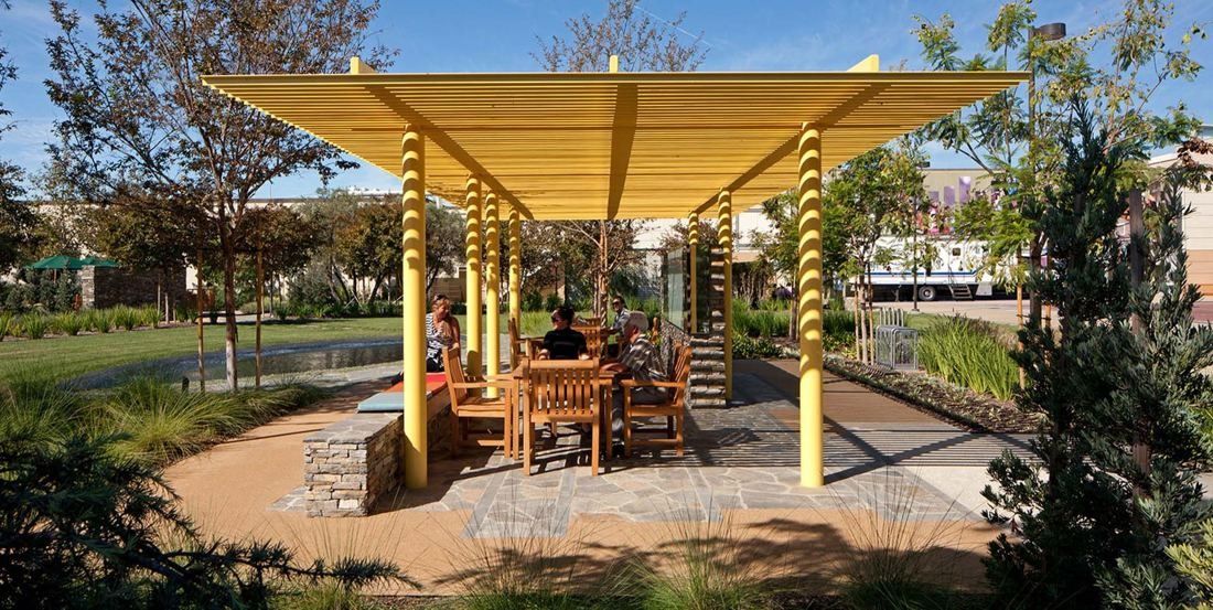 Amgen: Yellow slatted pavilion sheltering wooden tables beside a landscaped garden path