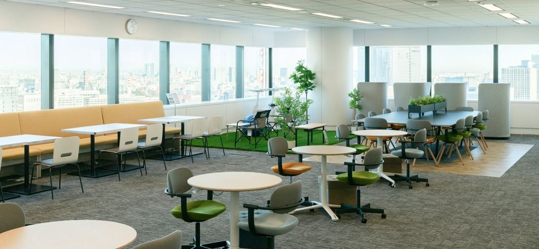 ANA: Bright open collaboration area with round tables, benches, plants and artificial grass beside tall windows