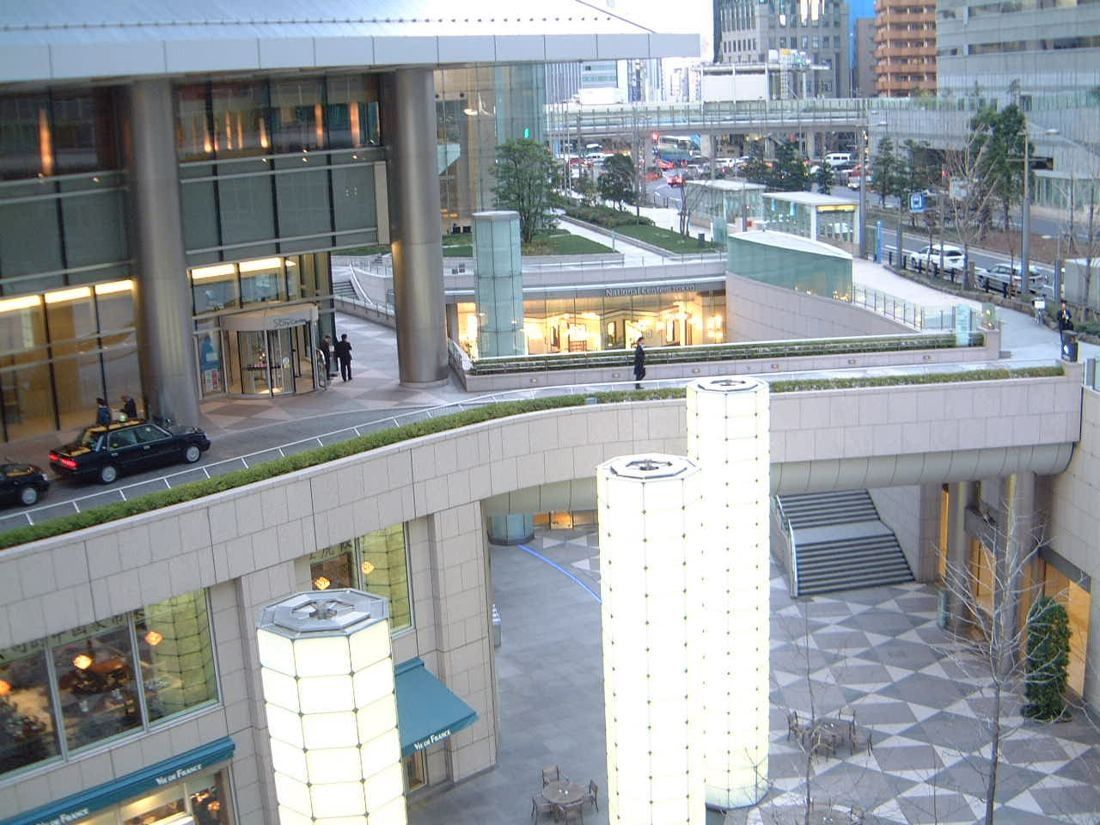 ANA: Elevated view of a sunken plaza with glowing columns, curved terraces and a taxi drop-off