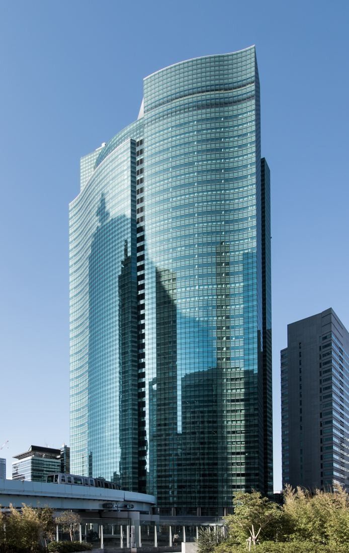 ANA: Green glass skyscraper with a curved top seen from below with lower buildings beside it