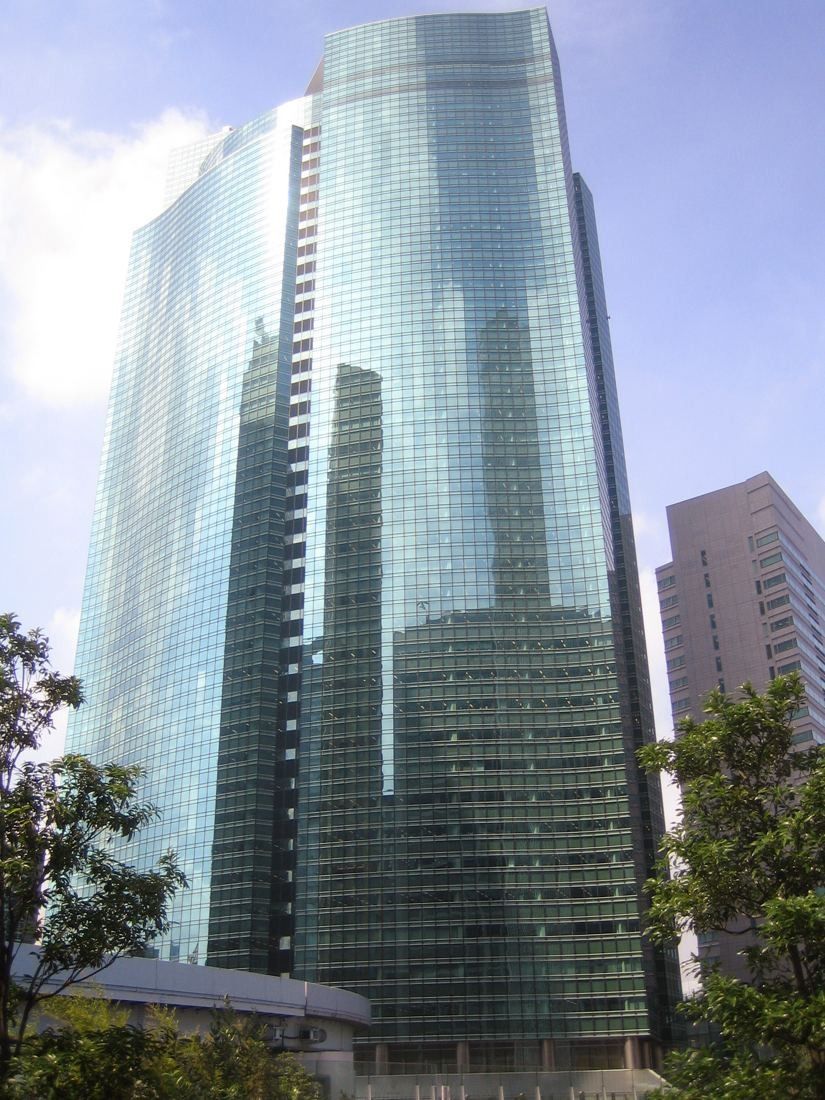 ANA: Green glass tower with a curved facade framed by trees and neighbouring buildings