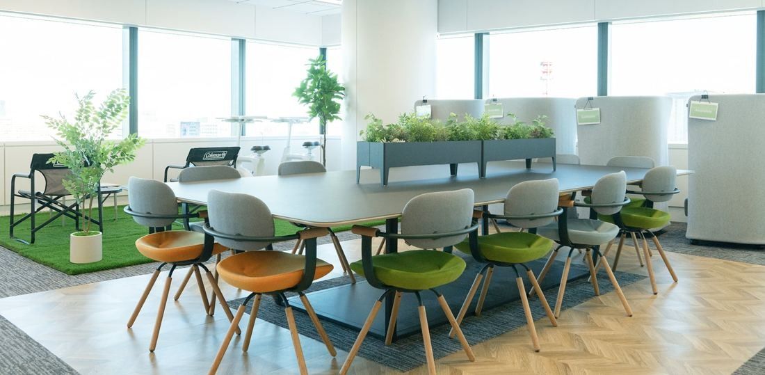 ANA: Large table with colourful chairs and planters on a herringbone wood floor by the windows