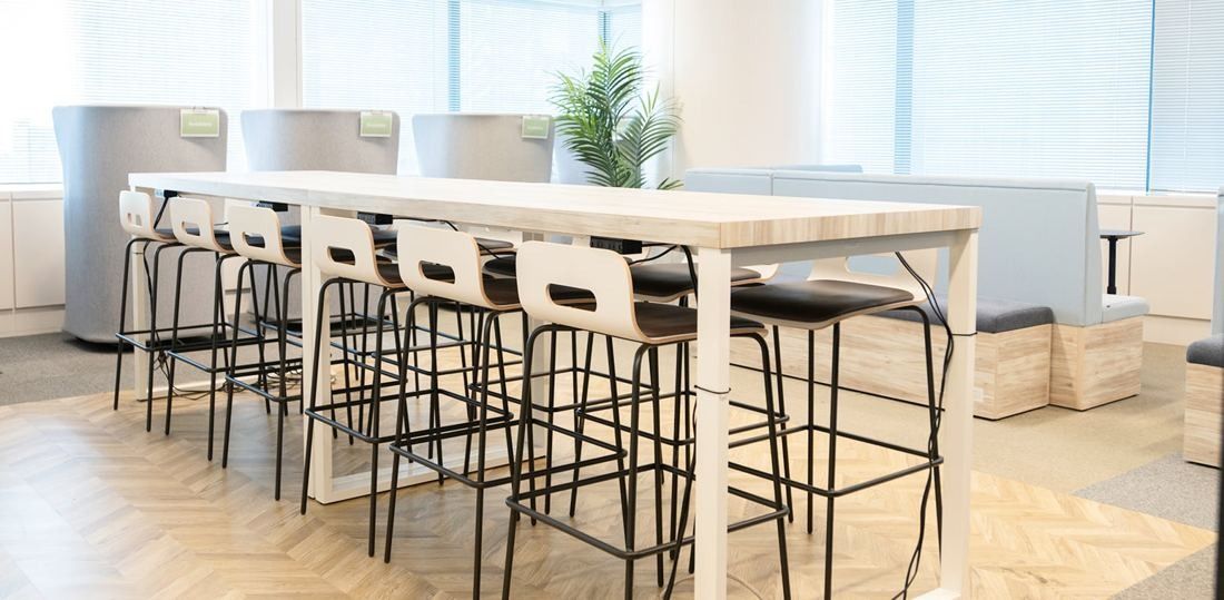 ANA: Long high table with bar stools on a herringbone floor in a bright lounge