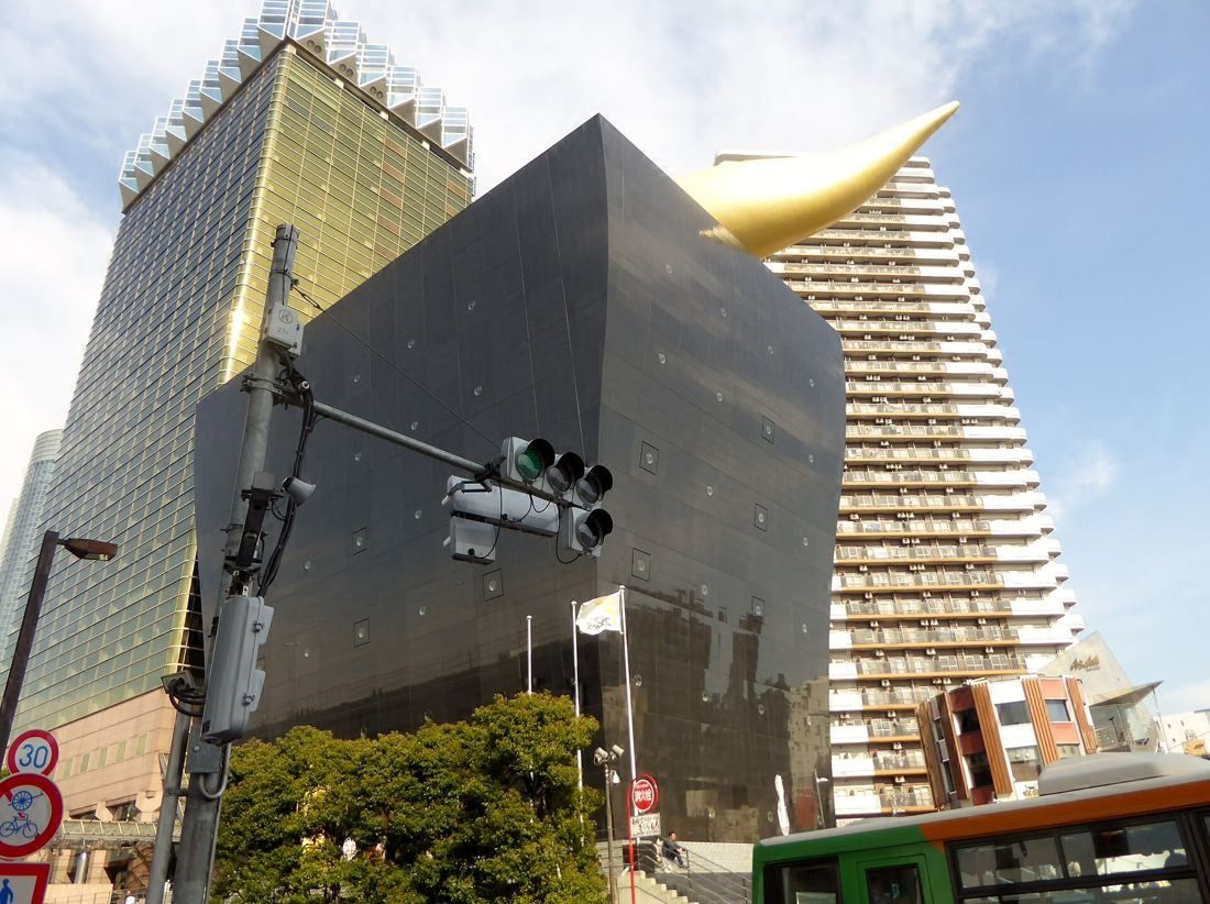 Asahi Group Holdings: Black hall with the golden flame and the gold tower seen at a street crossing