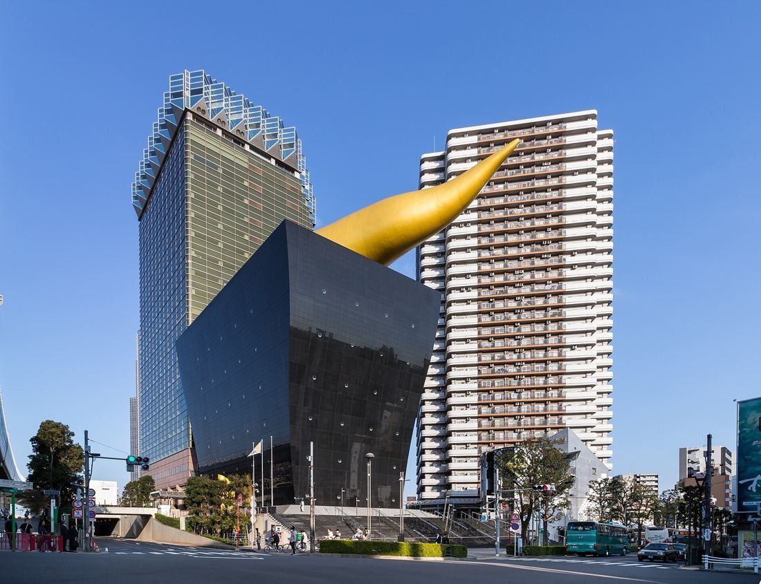 Asahi Group Holdings: Black tapered hall with a golden flame on its roof, in front of the gold tower, seen from street level