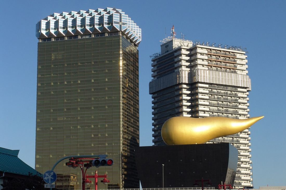 Asahi Group Holdings: Gold glass tower with its white crown next to the golden flame, seen from a street corner