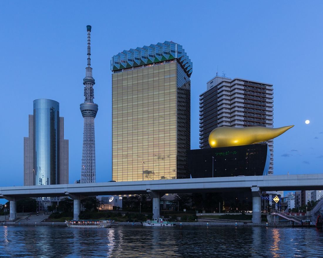 Asahi Group Holdings: Gold tower and golden flame with Tokyo Skytree behind, seen across the river in the evening