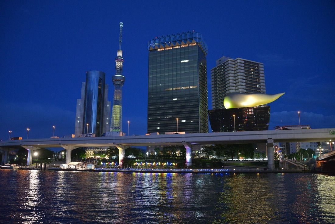 Asahi Group Holdings: Lit tower, golden flame and Tokyo Skytree at dusk, reflected in the river