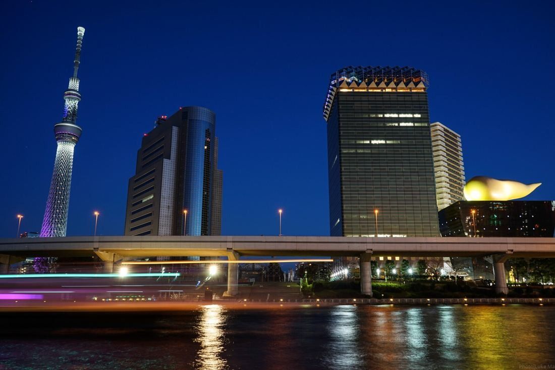 Asahi Group Holdings: Night view of the lit tower, flame and Skytree with light trails on the river