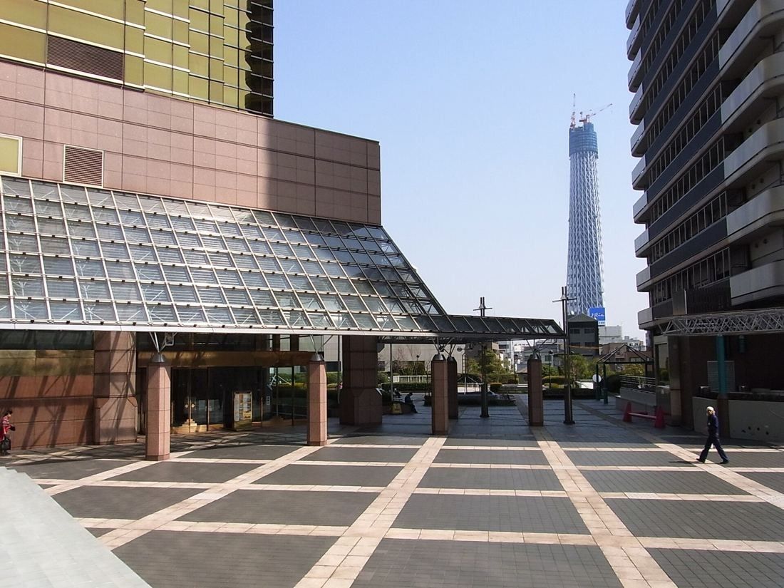 Asahi Group Holdings: Paved plaza with a glass canopy between buildings, Tokyo Skytree in the distance