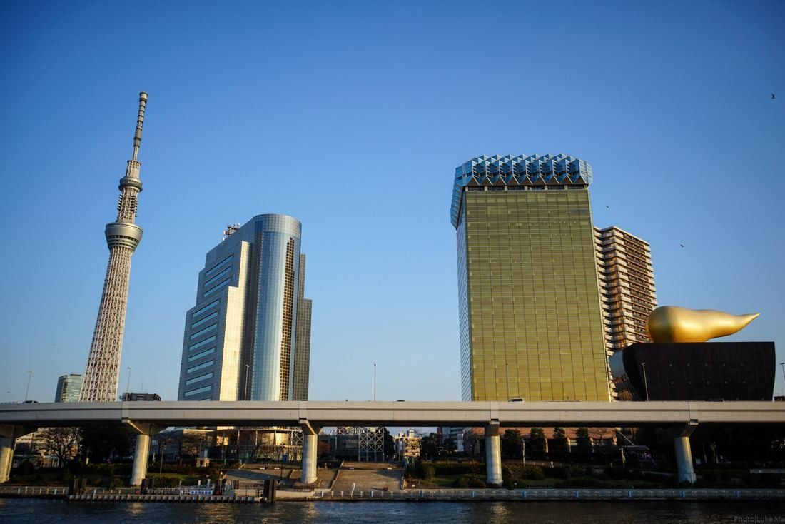 Asahi Group Holdings: Tokyo Skytree, a cylindrical glass tower and the gold tower in a row along the river
