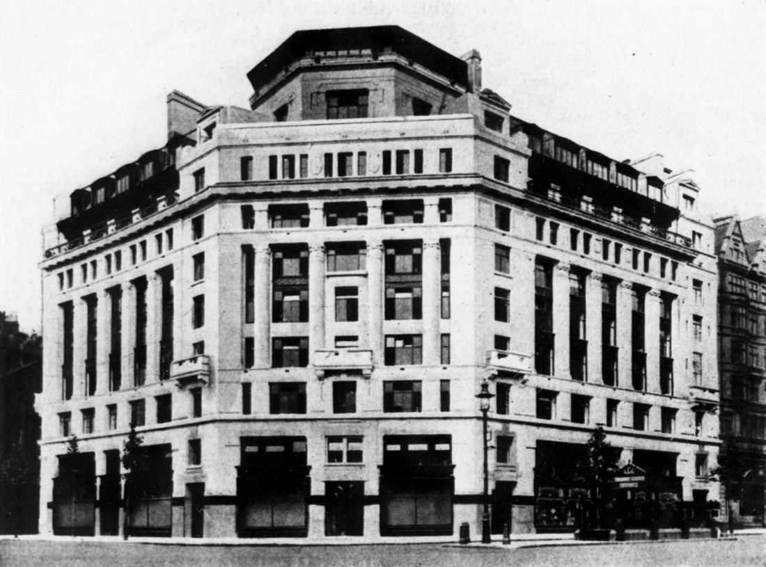 Black-and-white photograph of a large stone corner office block with a domed roof