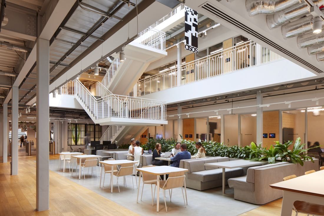 ASOS: Café seating with tables, banquettes and planters beneath white stairs and balconies