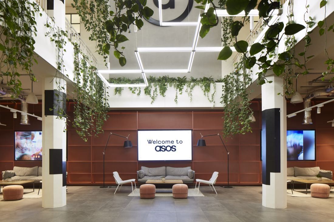 ASOS: Reception area with sofas, red panelled wall, screens and hanging plants under rectangular light fittings