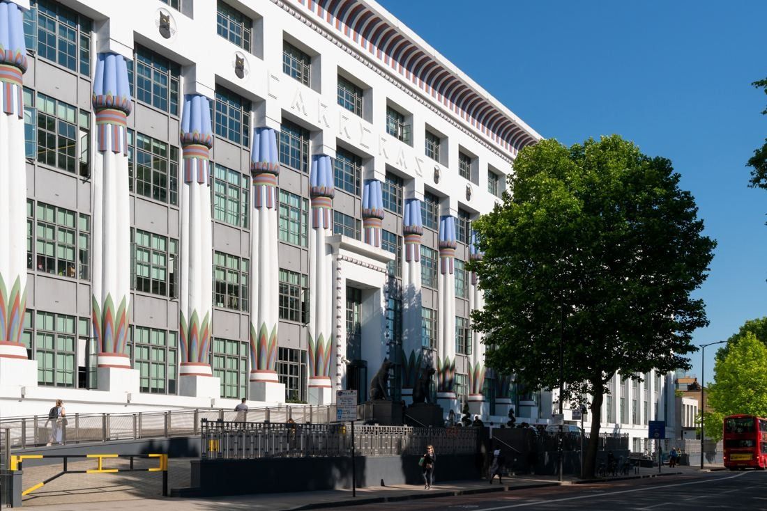 White Art Deco factory facade with coloured column capitals behind street trees under a blue sky