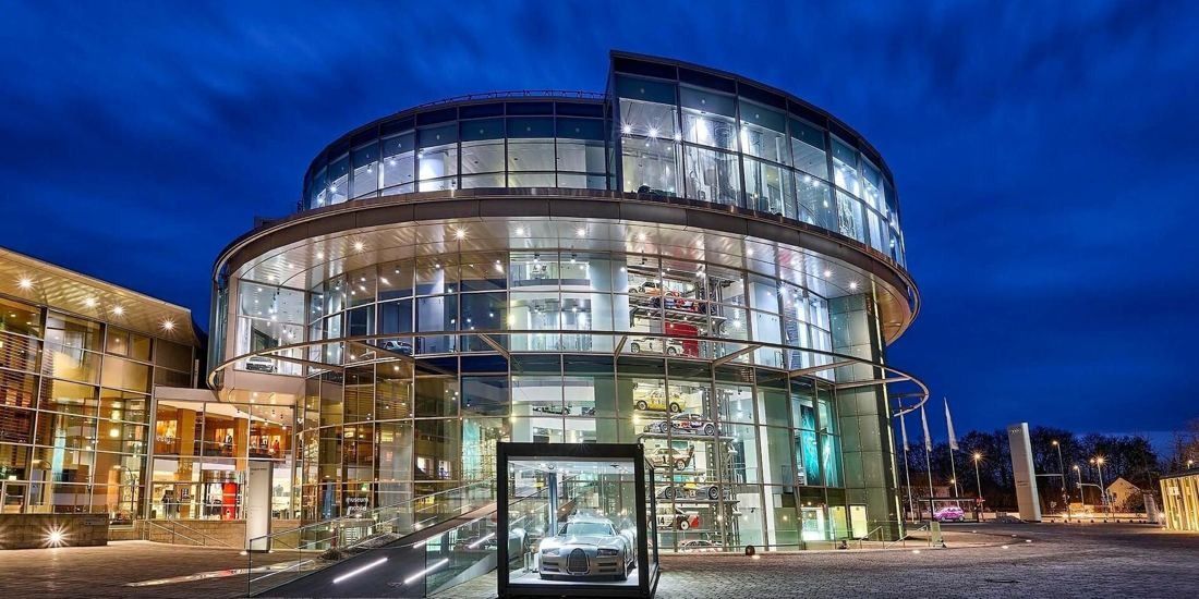 Audi: Curved glass building glowing at night under a deep blue sky