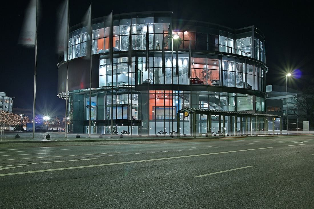 Audi: Glass rotunda lit at night across an empty street