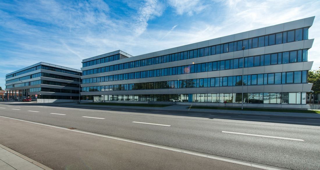 Audi: Long, low office buildings with stepped glass facades beside a road under a blue sky