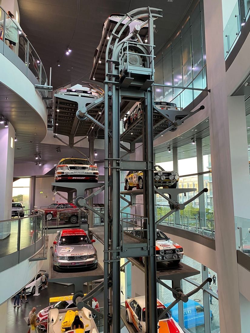 Audi: Vertical steel tower of stacked platforms holding cars inside a tall glass hall