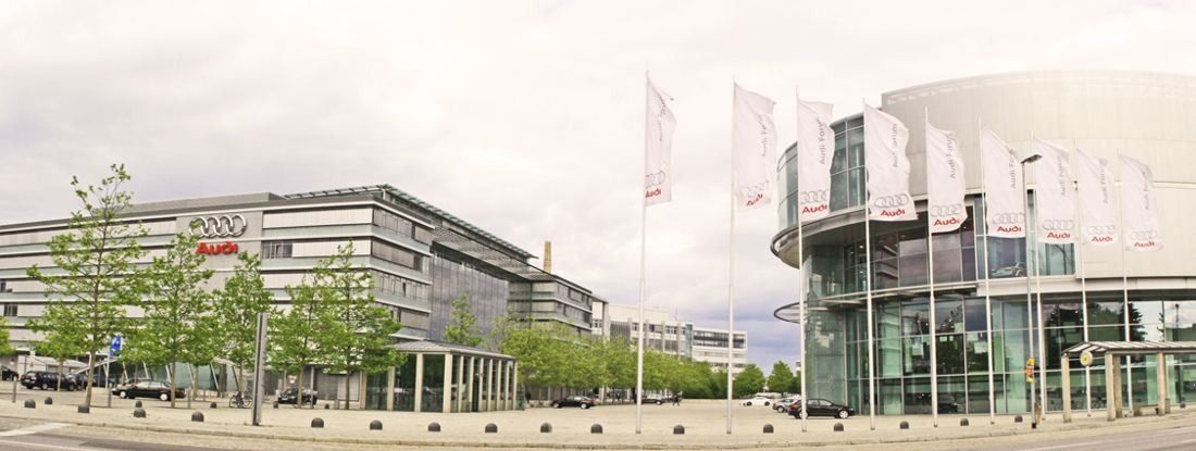 Audi: Wide view of office buildings, flags and a round glass building behind a landscaped entrance