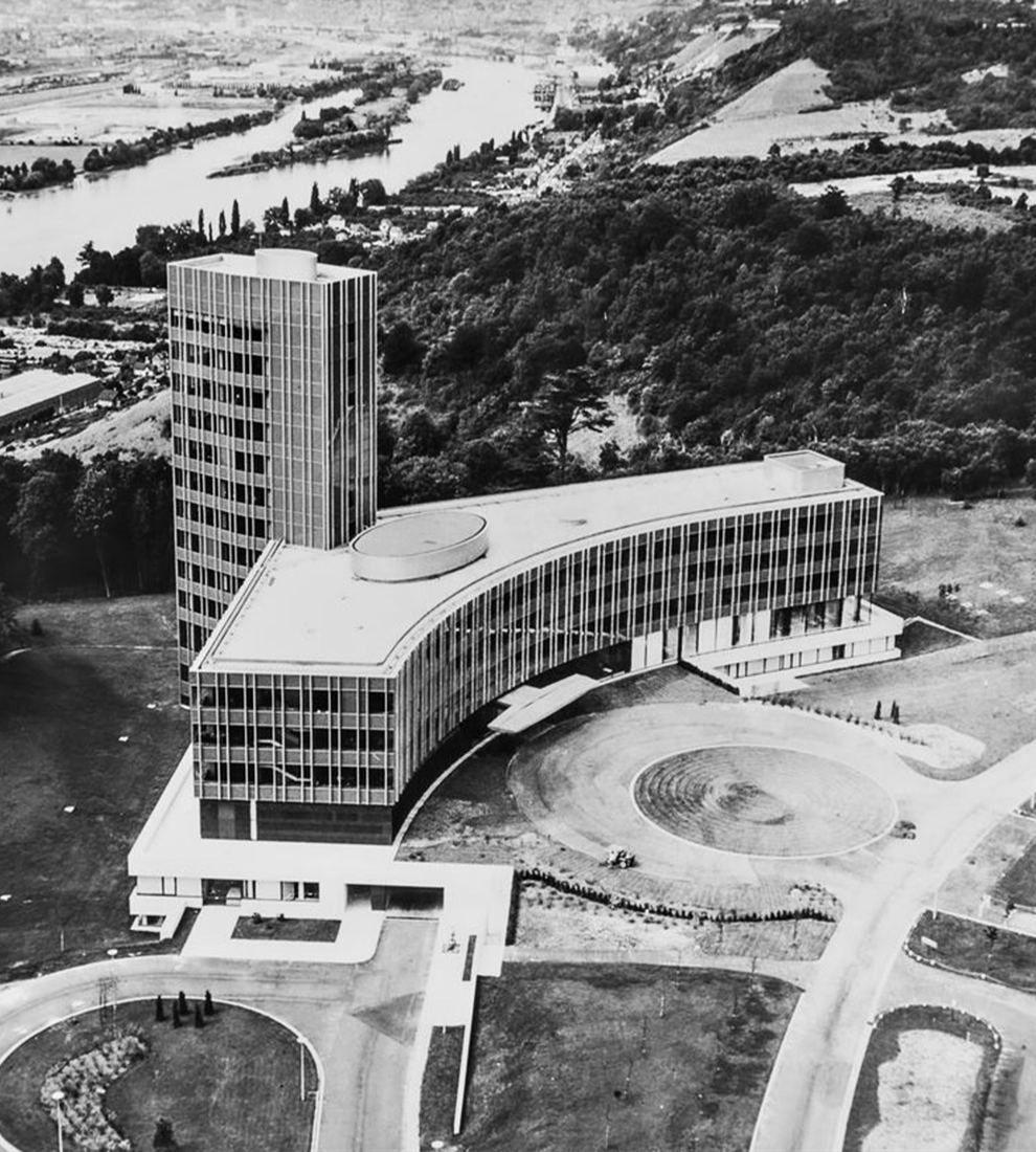 Black-and-white aerial view of an office tower and a curved low block above a river valley