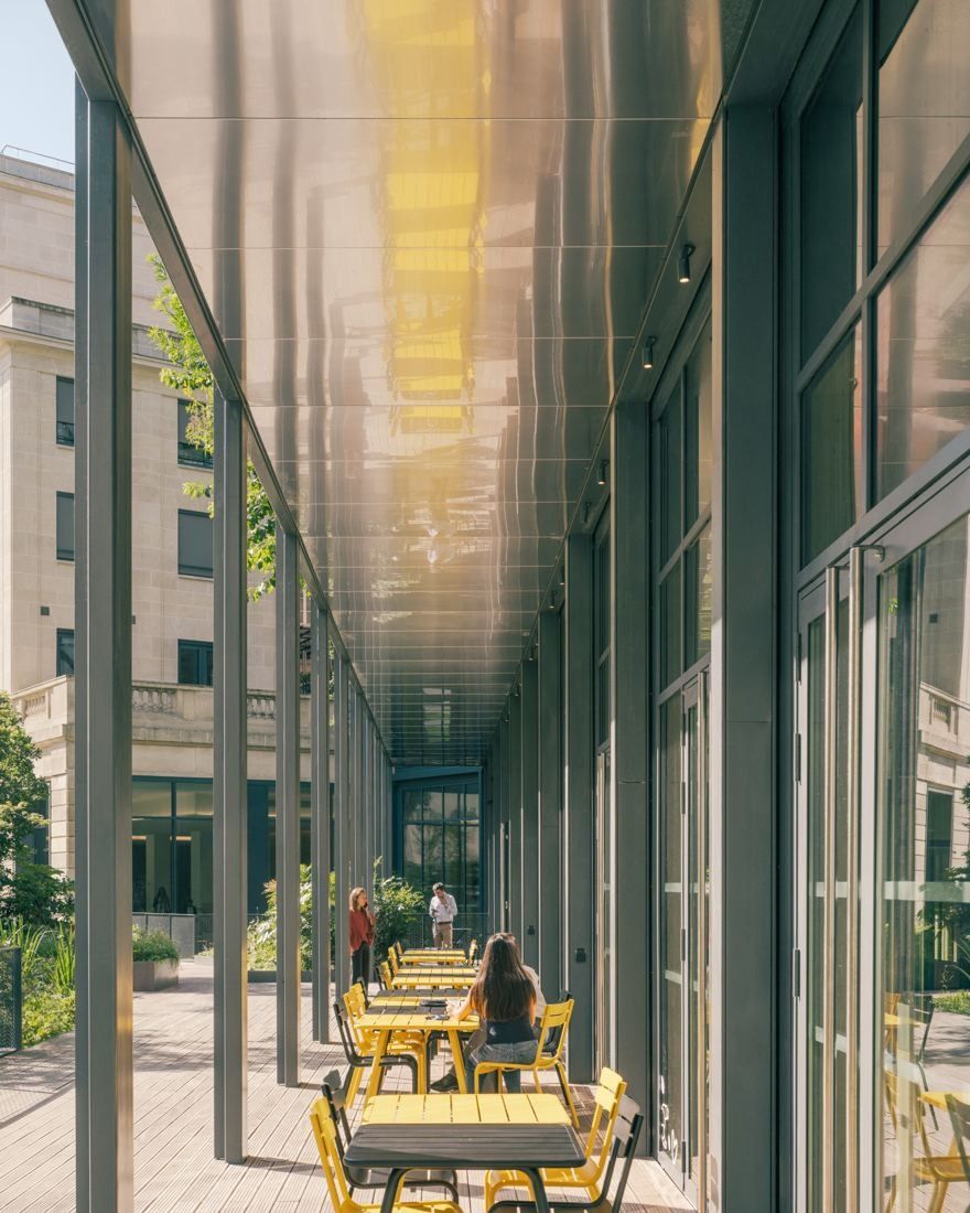 AXA: Covered outdoor gallery with yellow chairs and tables along a glazed façade