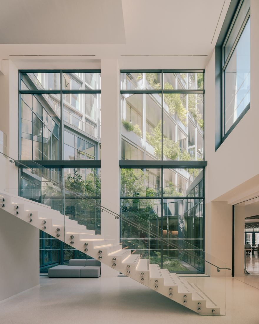AXA: Double-height white space with a floating staircase and tall green-framed windows